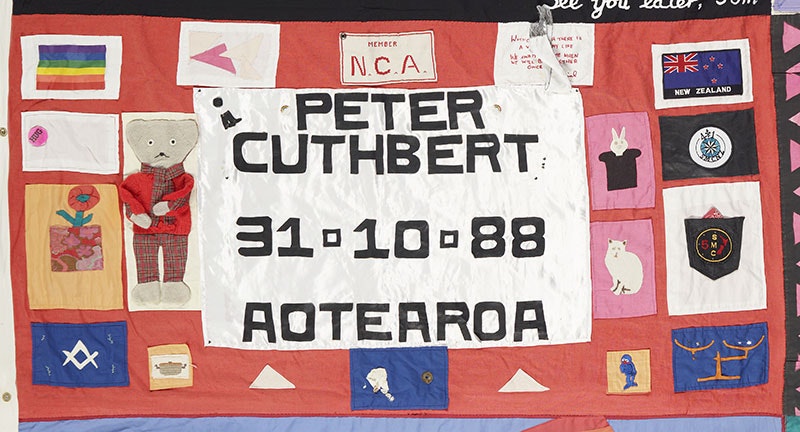 Panel of the NZ AIDS Memorial Quilt. It is predominantly red and comprises of many mini patches and the words ‘Peter Cuthbert 31-10-88 Aotearoa’