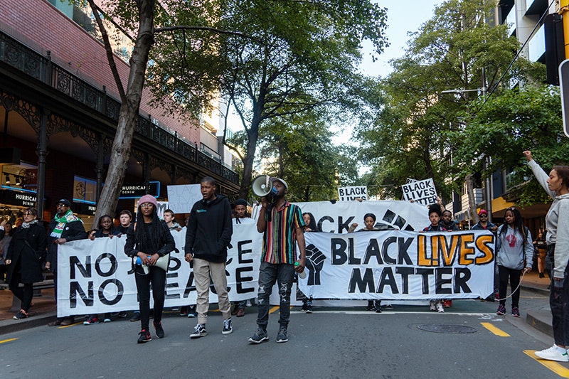People in front of a Black Lives Matter banner marching in a tree-lined street