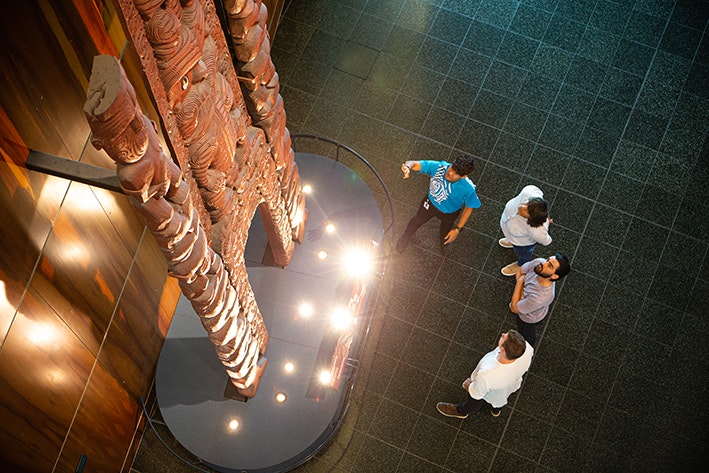 Four people standing in front of a wooden carving in a large space