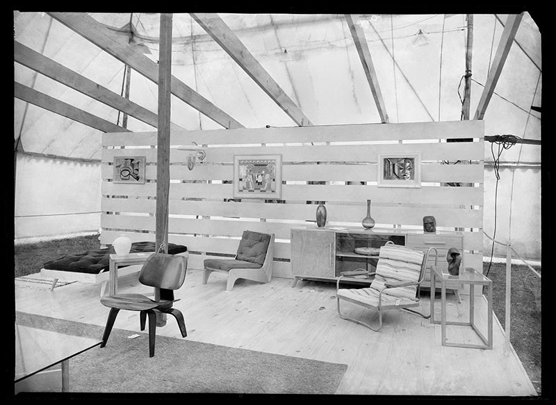 Display of a mid-century living room set up in an exhibition, with chairs, painting on the wall, and a sideboard