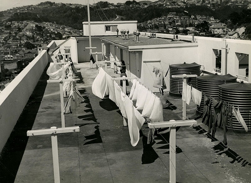 Black and white photo of a woman hanging out the washing on the roof of an apartment complex