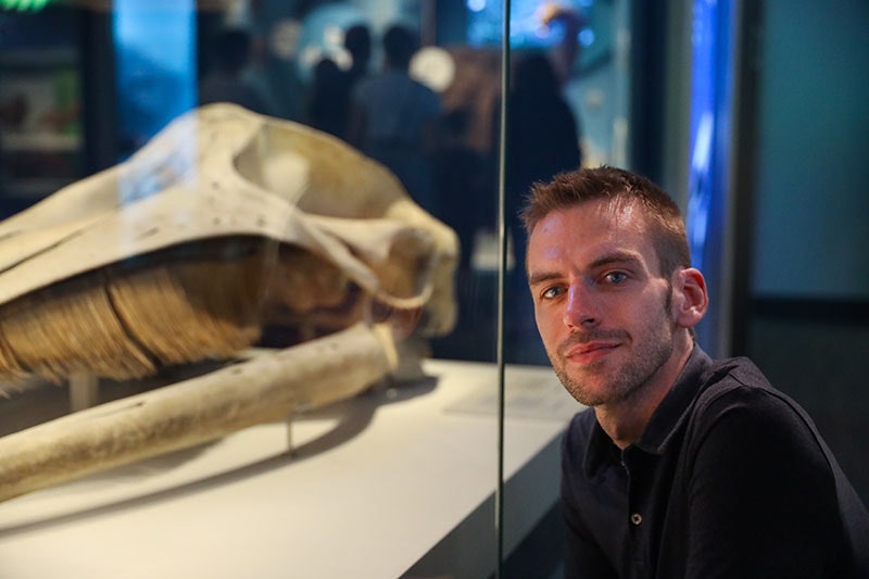 Man poses for a photo beside the skull of a whale