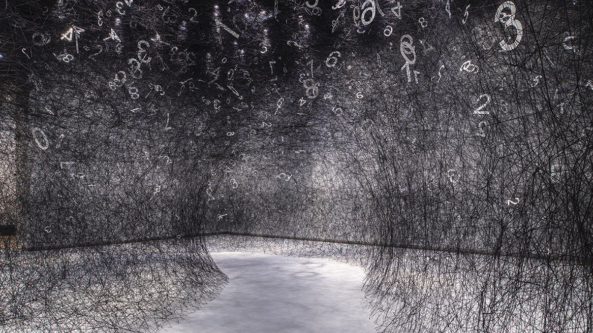 Black wool in a web stretched across a museum gallery floor, with white numbers sitting in random parts of it.