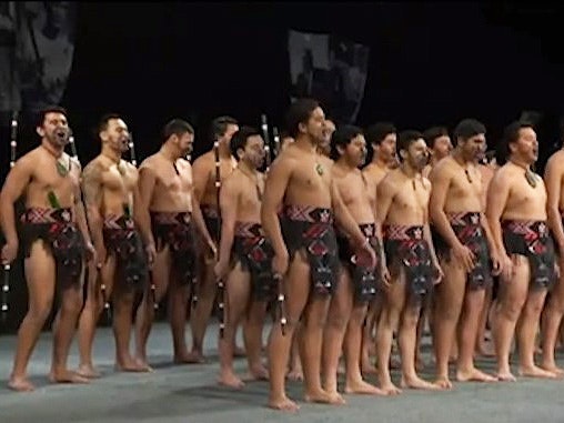 A group of young men singing on stage in traditional Māori dress