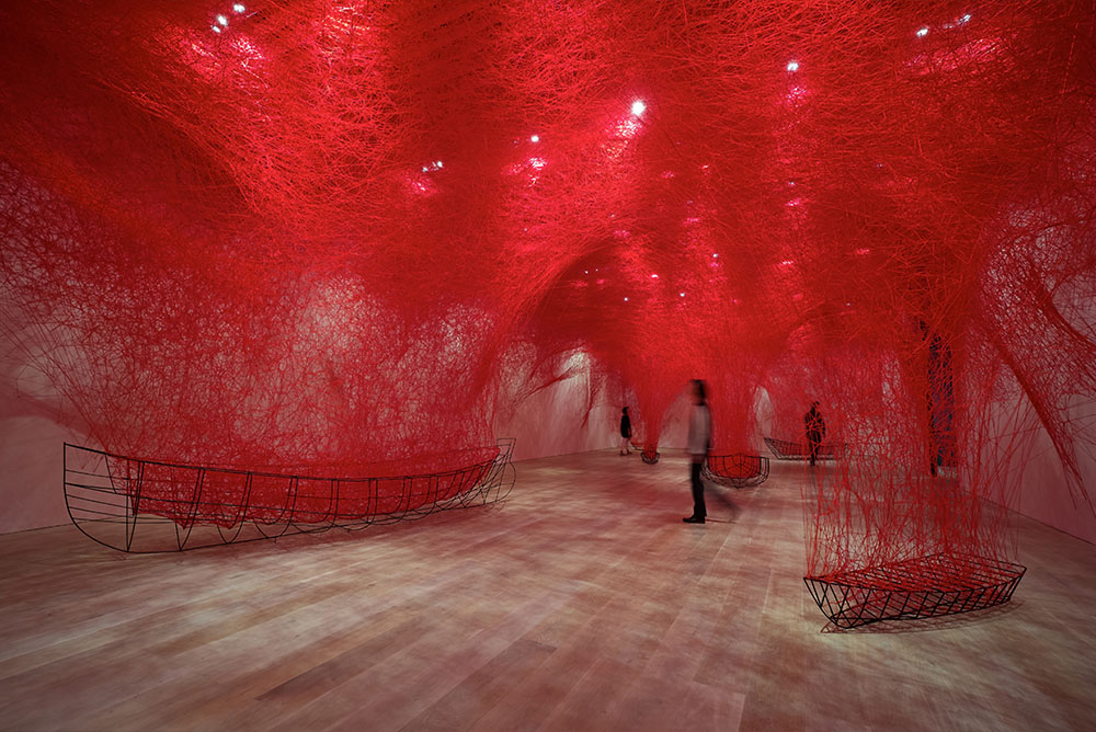 A room full of black wire framed boats filled with red wool suspended like a web from the ceiling