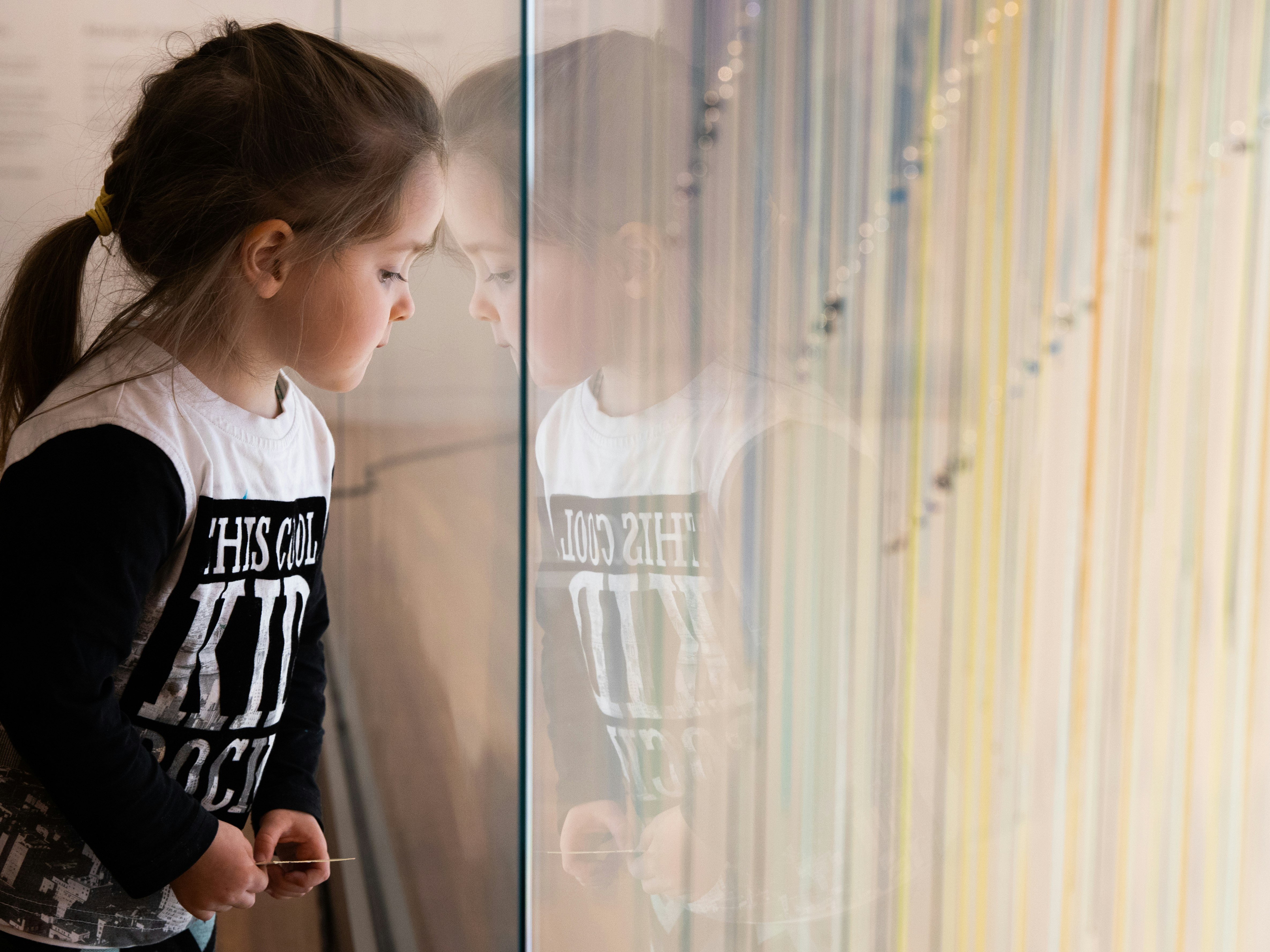Toi Art balustrade. Photo by Jack Fisher. Te Papa Child sitting next to a glass wall looking at coloured ribbons