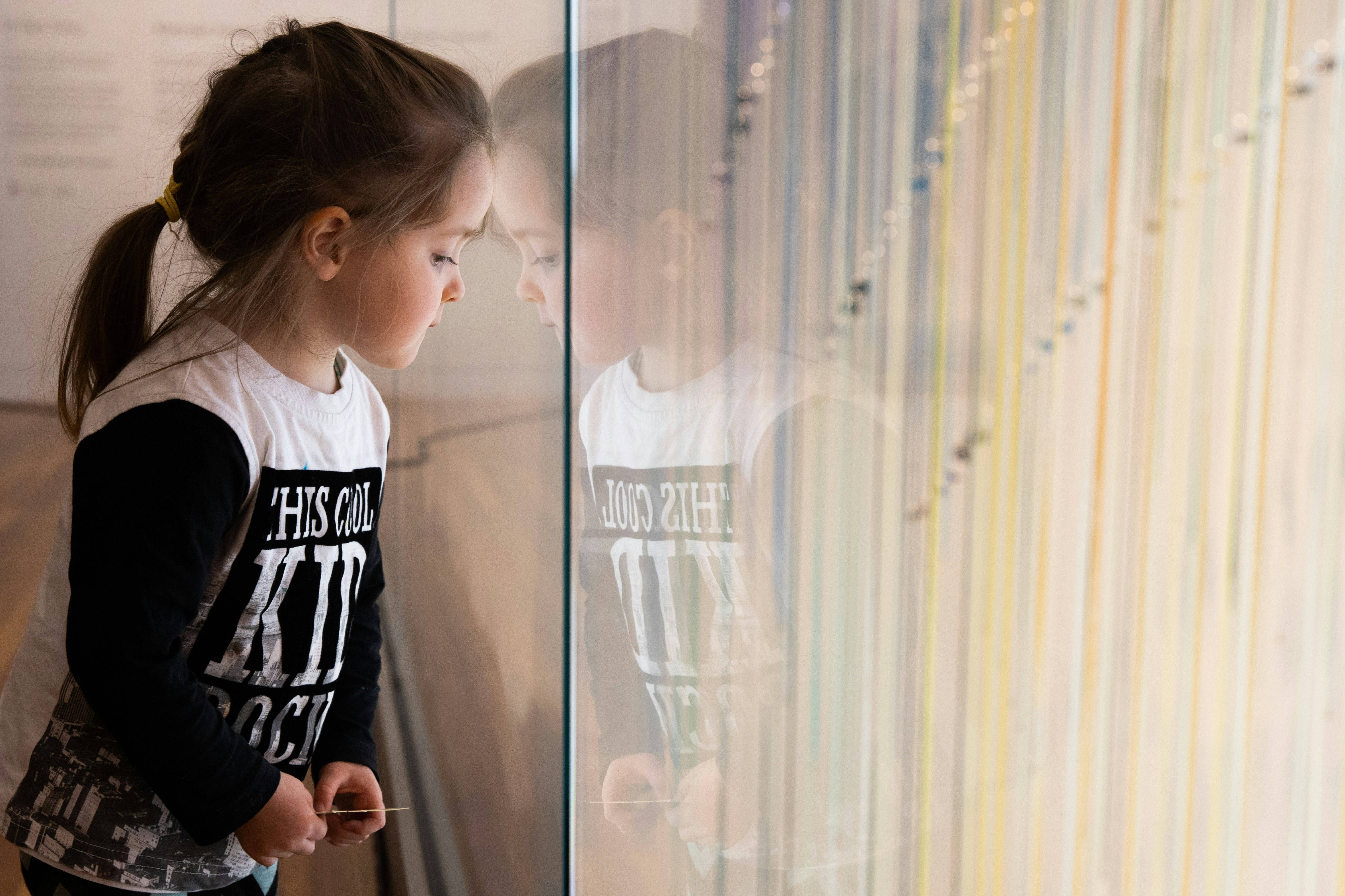 Child sitting next to a glass wall looking at coloured ribbons
