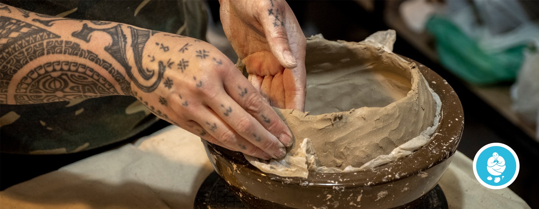 Tattooed hands on a clay pot on a wheel
