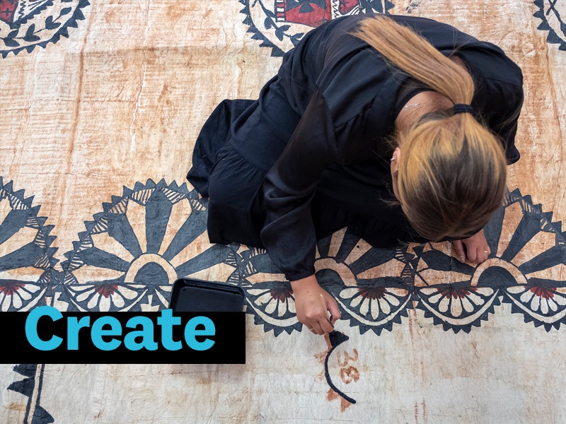 A woman crouching on a tapa cloth painting with black paint