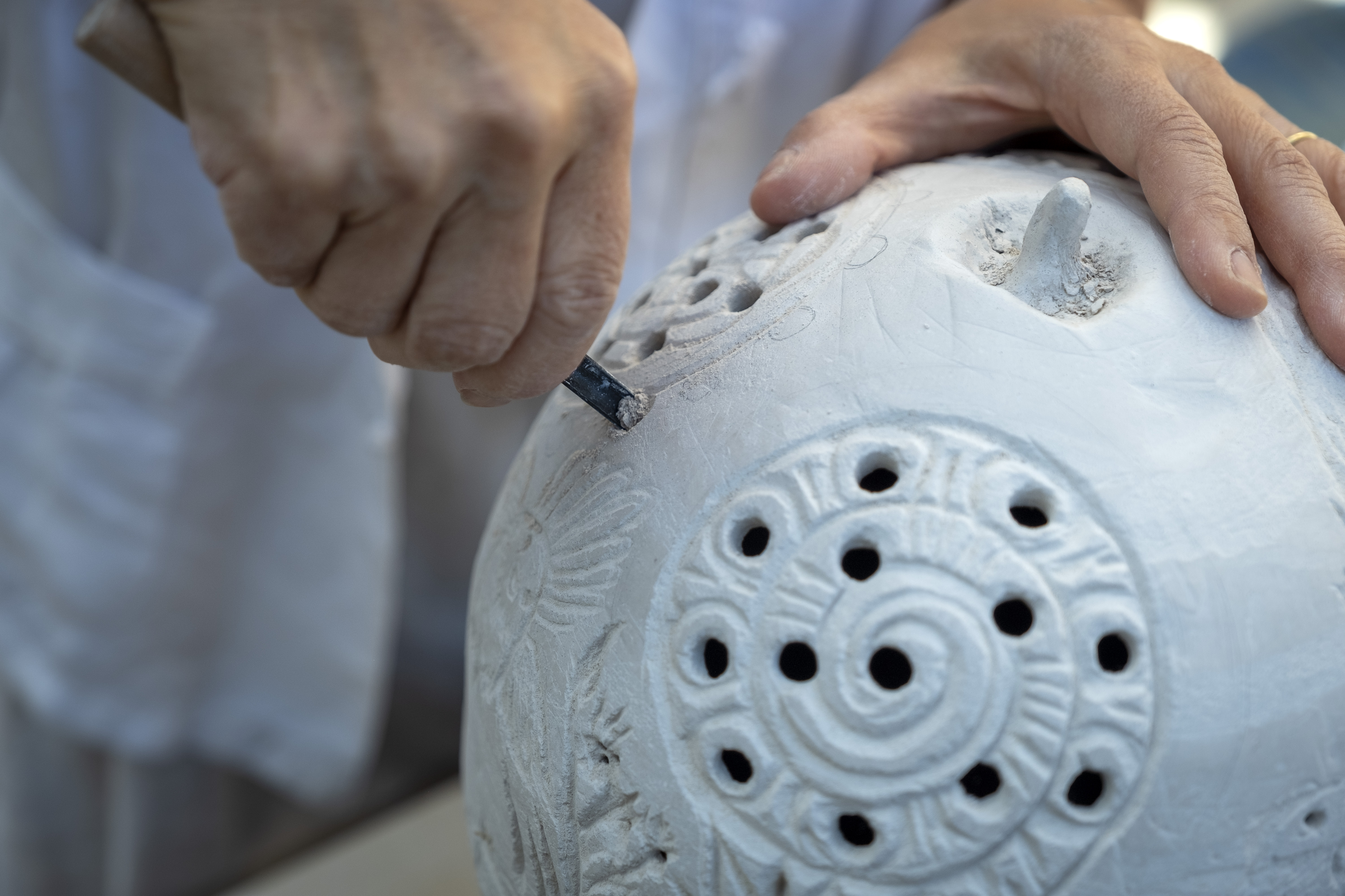 Two hands working on a piece of unfired clay pottery.