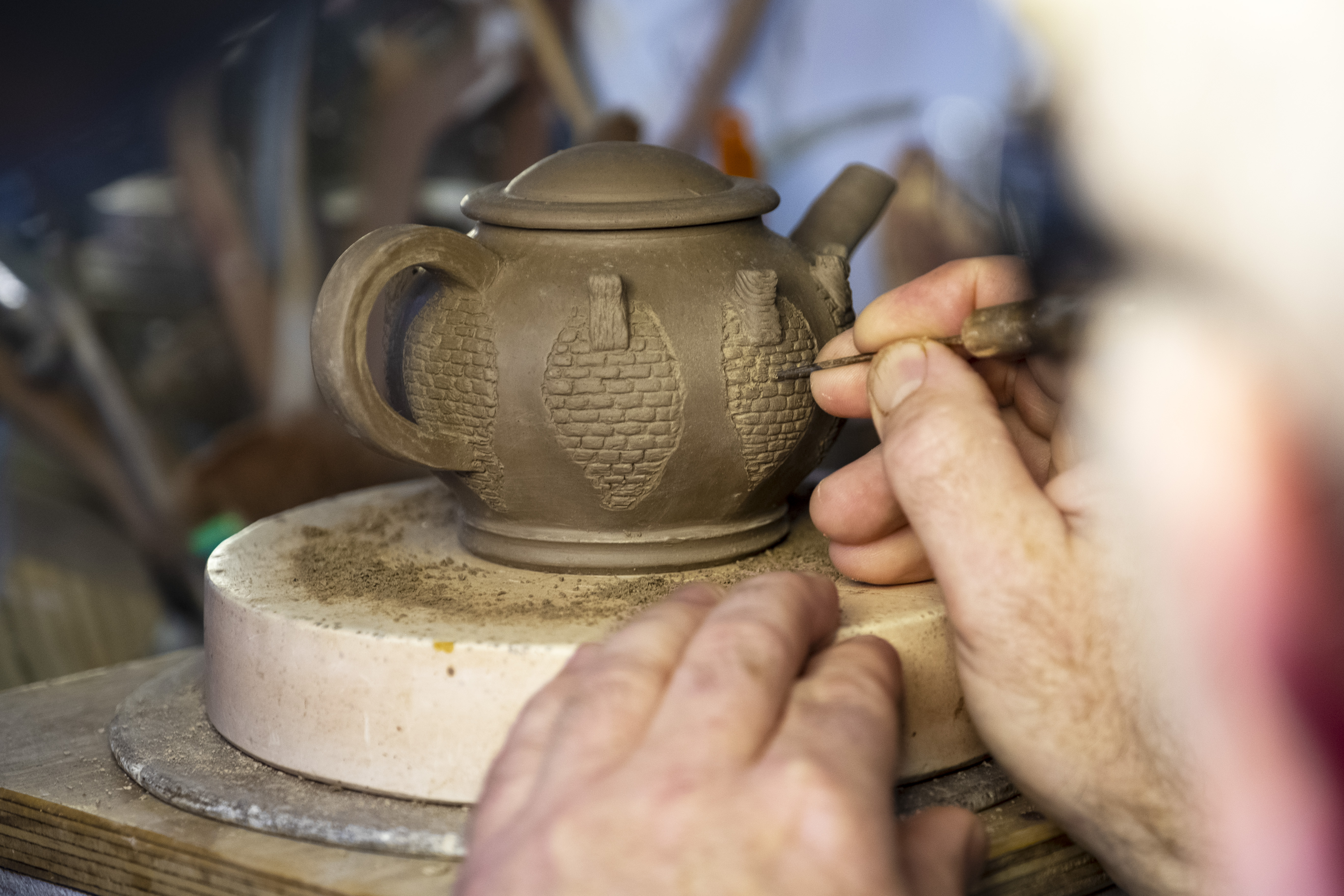 Two hands working on a piece of unfired clay pottery.