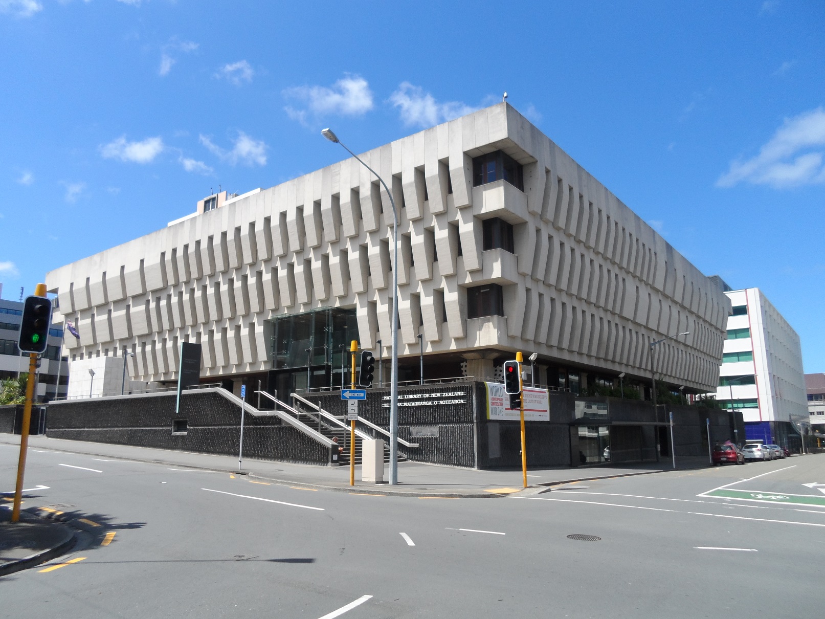 A large black and white building on the corner of a street. There are street lights on the corner