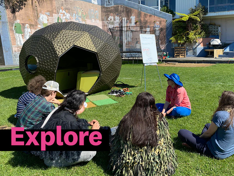 People sitting on a lawn in front of a large shape that looks like a bronze egg