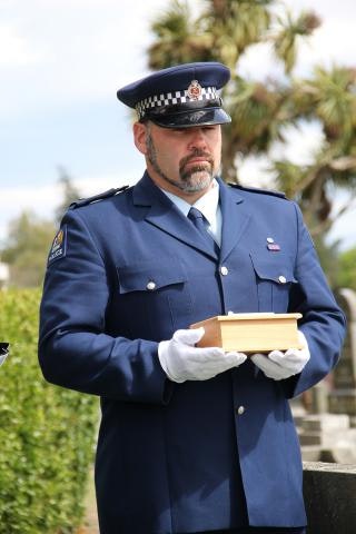 A man in police uniform holds a small wooden box