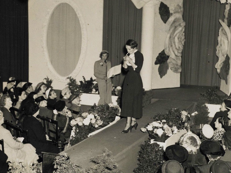A black and white photo of a woman lighting up a cigarette on the catwalk