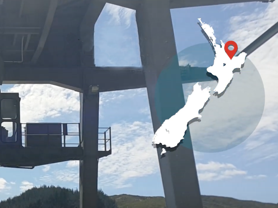 A steel structure with blue sky behind and a map of New Zealand overlaid on the right-hand corner