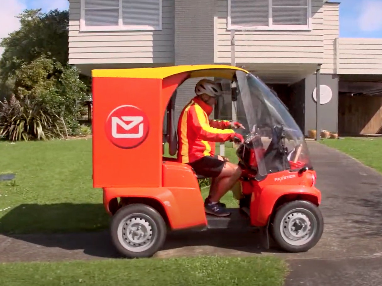 A person driving a red and yellow electric vehicle in front of a house