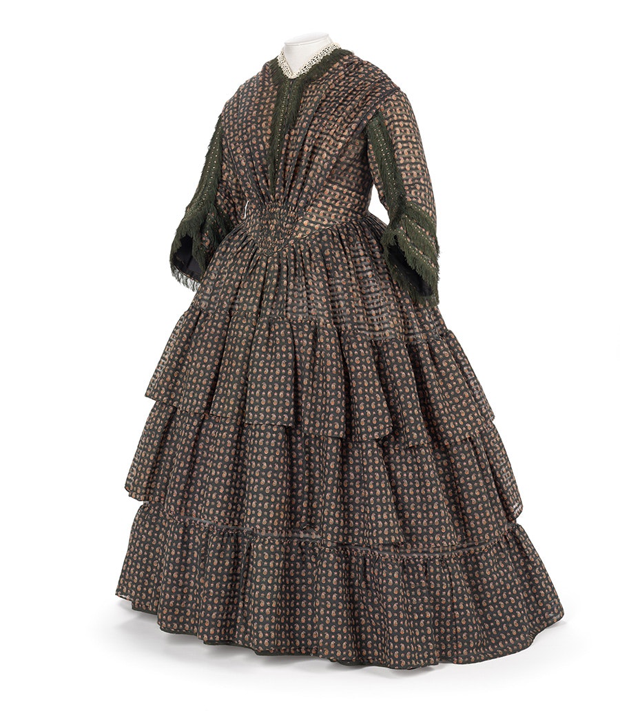 A dark green and red 1850s dress on a mannequin with a white background