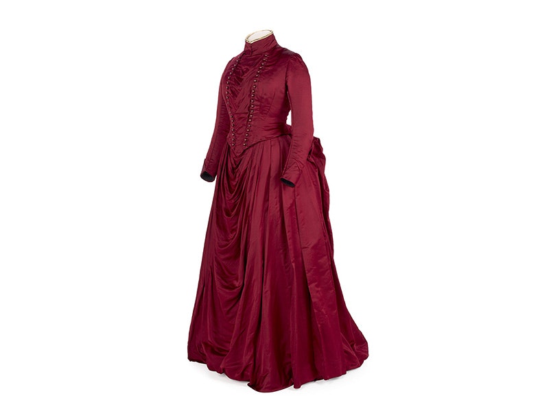 A red 1880s silk dress with a bustle on a white background