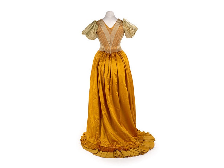 A full-length yellow silk dress from the 1890s on a white background