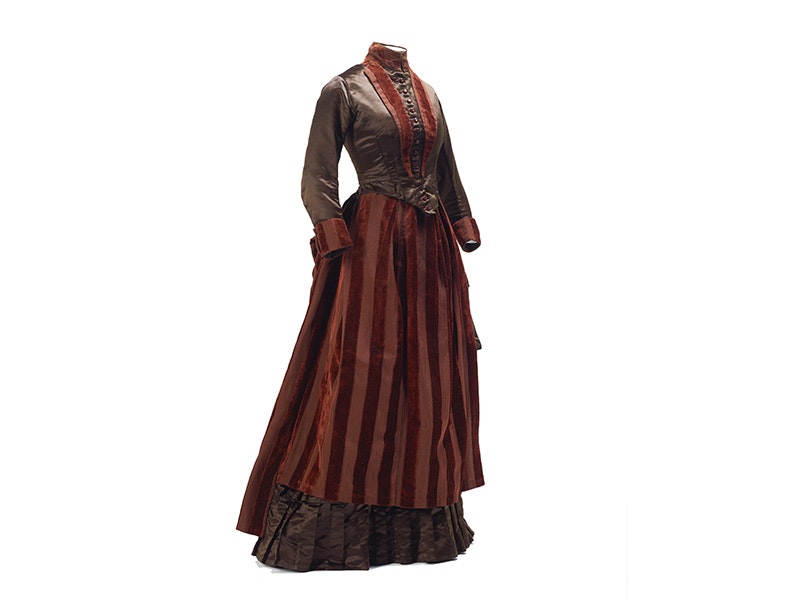 A brown silk and velvet 1880s dress with a white background.