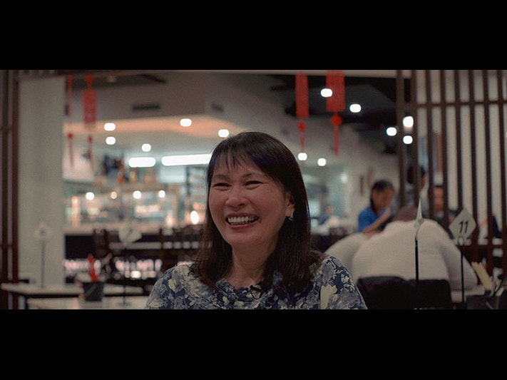 Still from the video of Tee at Little Penang, 2021. Photo by Arthur Hon Sheng. Te Papa A woman smiles as she talks to an interviewer off-screen