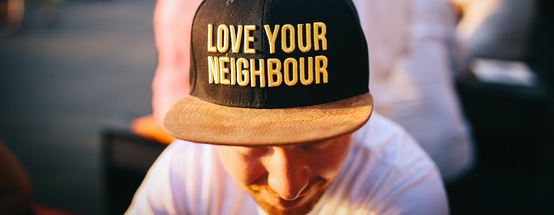 Close up of a man wearing a black cap. On the caps are the words ‘Love your neighbour’