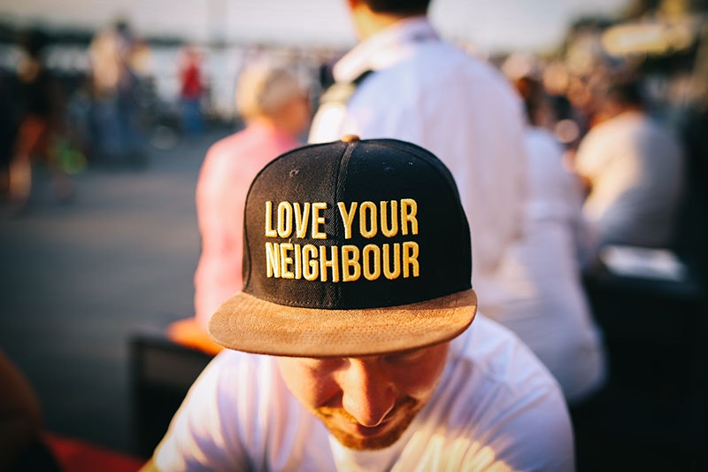 Close up of a man wearing a black cap. On the caps are the words ‘Love your neighbour’