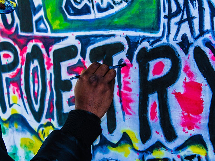 Text on wall that says “Poetry” being painted by a hand. Photo by Trust Katsande via Unsplash Text on wall that says “Poetry” being painted by a hand