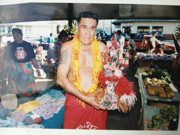 A man standing in a colourful market stall holding a feathered headdress