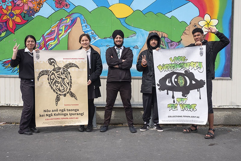Five students stand holding two large posters