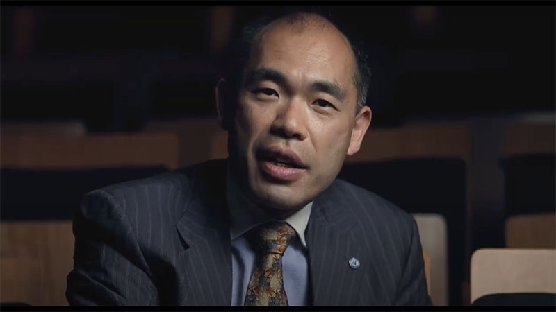 Henry Liu talks directly to camera in a darkened space