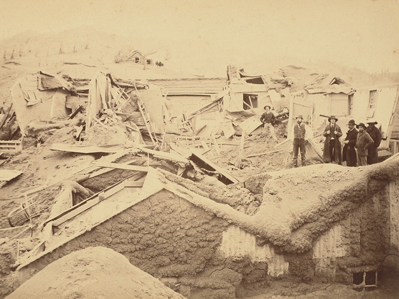 Sepia photo of two people standing on the ruins of a shed covered in mud