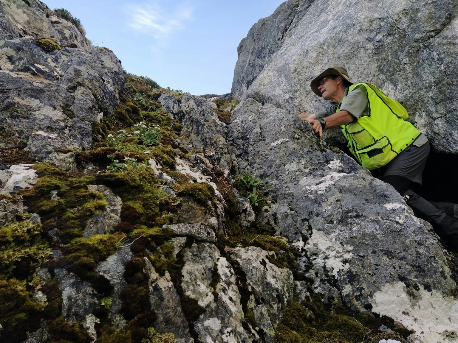 A man in high-vis gear leaning on a mountain rock