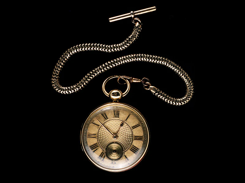 A pocket watch and chain on a black background