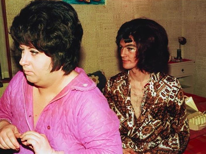 Fiona Clark, Tiny Tina and Ian Geraldine dress at home, Auckland, 1975, Auckland. Printed 2016. Te Papa (O.043776) Two men, wearing wigs, sitting on a bed get dressed. One wears a pink blouse and the other a brown shirt