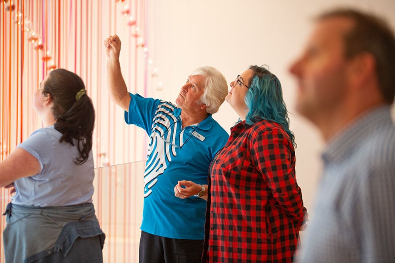 A Te Papa host talks to a visitor about an artwork representing a rainbow suspended from the ceiling
