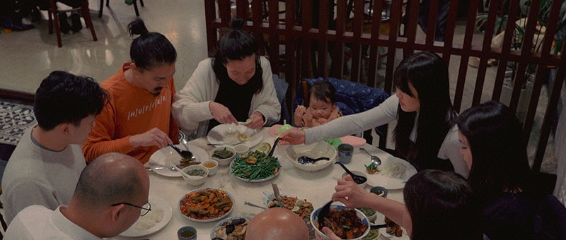 Nine people sit around a circular table eating a vast array of food, in a restaurant