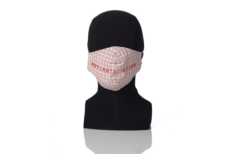 A pink mask on a mannequin head with the words "anti anti Asian" embroidered on it