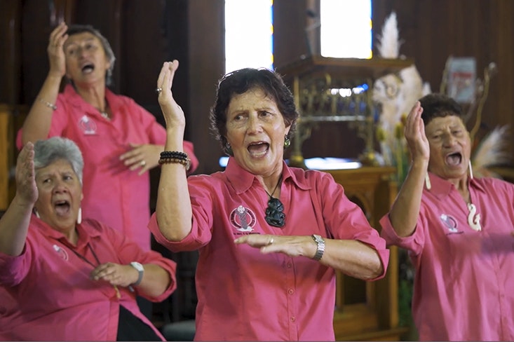 Four women in pink shirts singing with hand actions