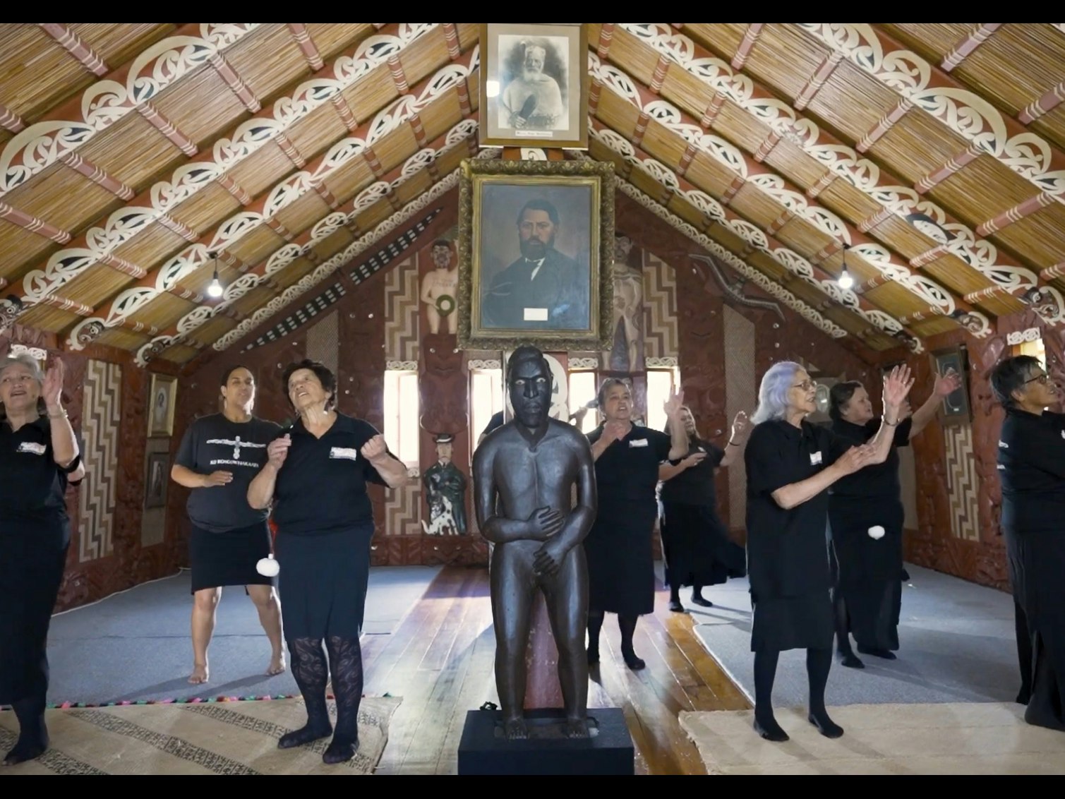 rongowhakaata_taikura.jpg A group of people singing and doing actions in a hall with carvings and painting on the rafters