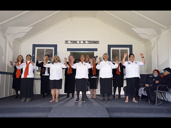 A video still from the Taikura Kapa Haka 2022 series A group of women are singing an action song on the front porch of a hall