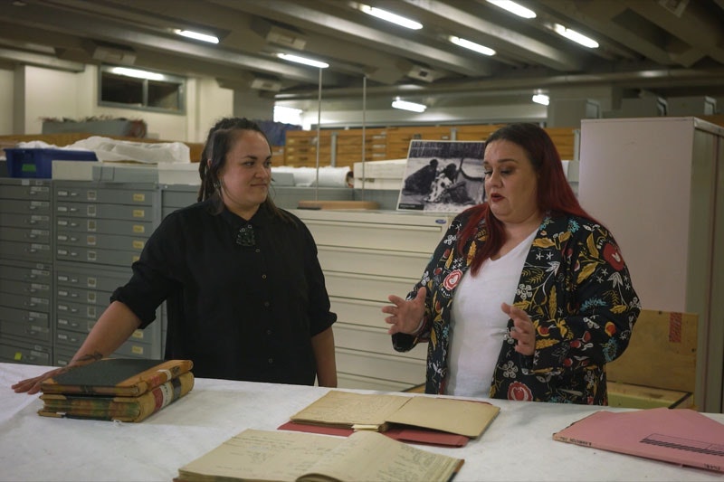 Two women stand talking in a museum storeroom, surrounded by storage cabinets