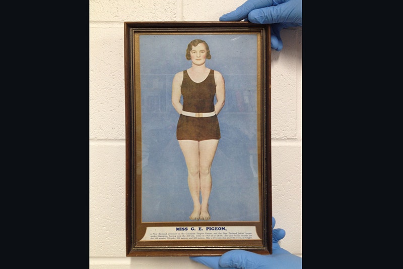 A pair of blue-gloved hands holds a framed colourised photo of a woman in a bathing costume.