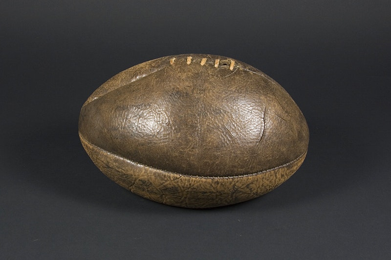 A brown leather rugby ball on a black background. The ball is slightly deflated.