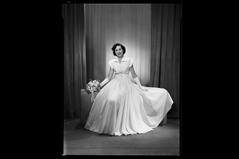 A black and white photo of a woman in a white dress sitting in a studio setting