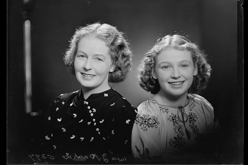 A studio portrait of a woman and a girl sitting next to each other and smiling at the camera