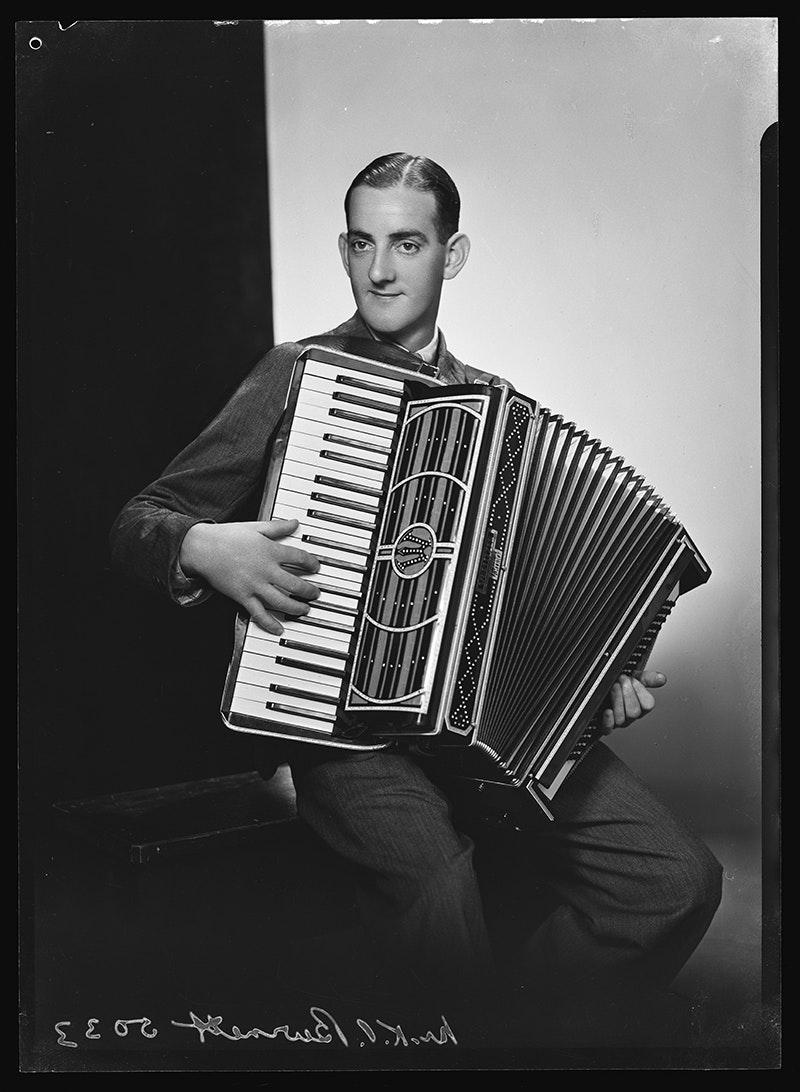 A black and white studio photo of a man playing an accordion