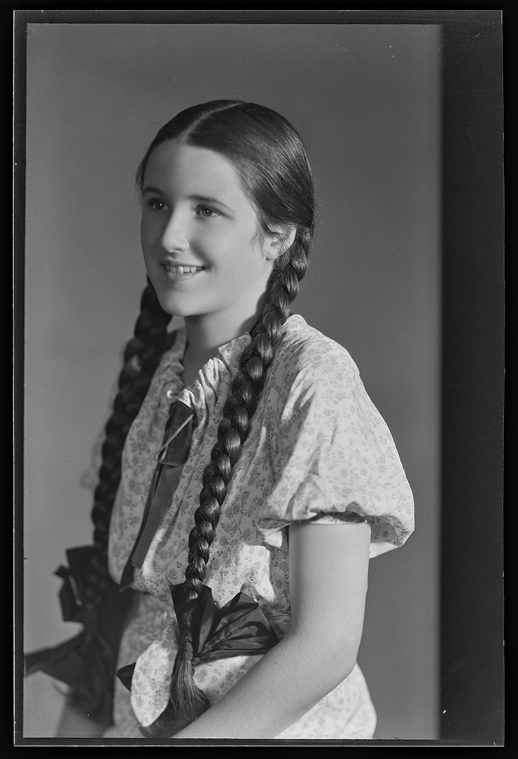 A black and white photo of a young girl with long hair sitting in a photographic studio