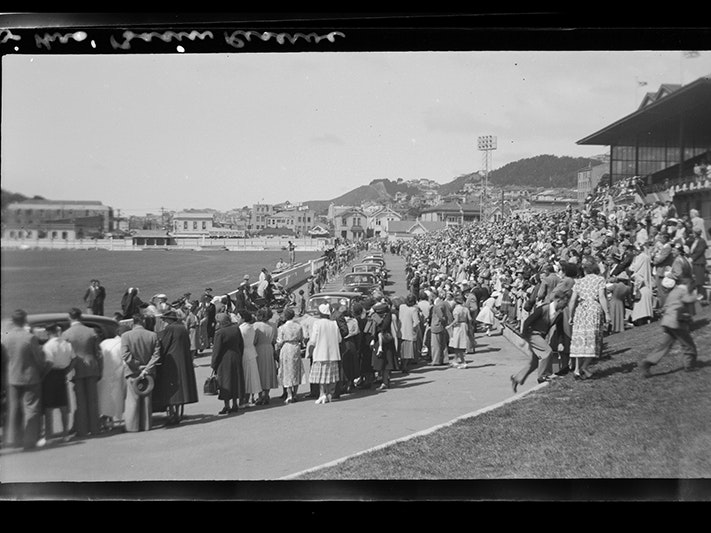 Queen's visit, December 1953-January 1954 ..., 16 January 1954, by Leslie Adkin. Te Papa (A.008487) A lot of people in a stadium field waving as a motorcade passes by